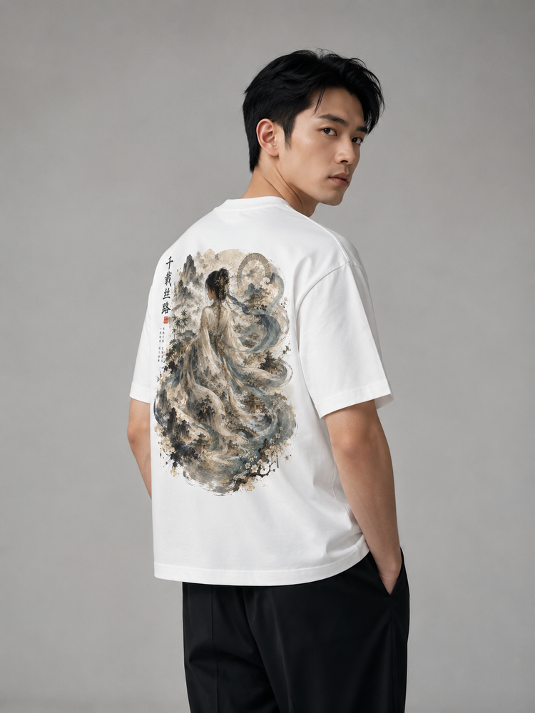 A man wearing a white short-sleeve T-shirt with a large traditional Chinese ink-wash style print on the back, paired with black pants, photographed against a neutral gray studio background.