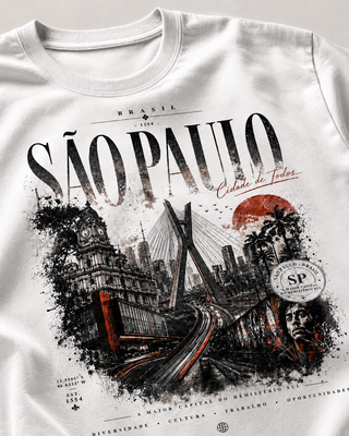 White crewneck t-shirt featuring a detailed graphic print of São Paulo, Brazil, with black ink cityscape illustration, a red sun, and the text 'SÃO PAULO' and 'Cidade de Todos'.