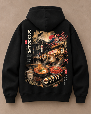 A black pullover hoodie shown from the back, featuring a large detailed graphic print of a Korean street food scene with bowls of soup, sushi, hot dogs, cherry blossoms, a moon and sun, and vertical text reading KOREA.
